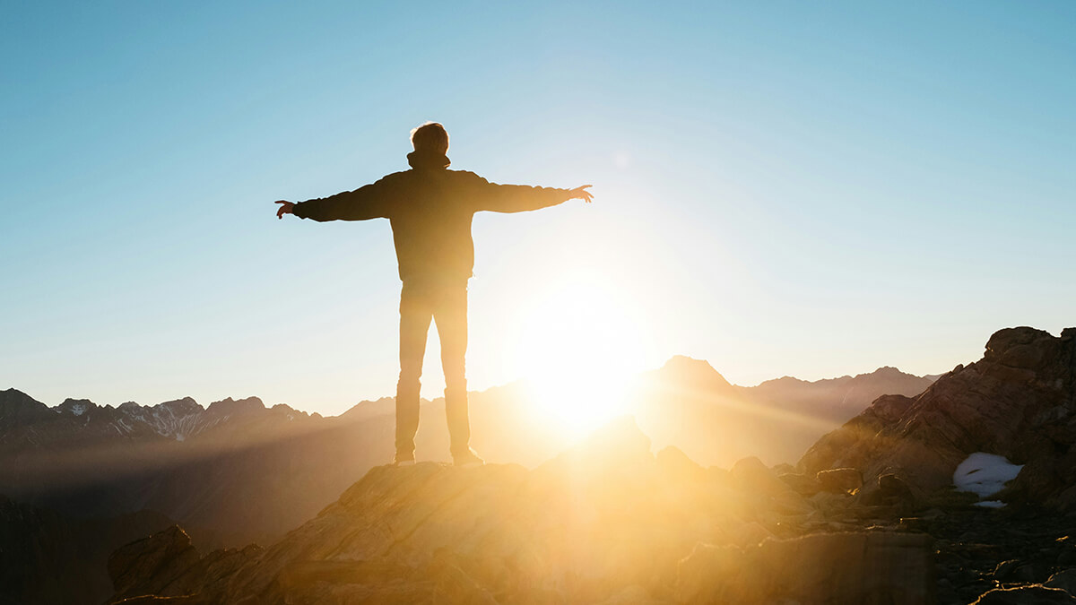 A person stands at the top of a mountain with their arms extended