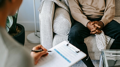 A doctor and patient sitting in an office while the doctor fills out a clipboard.