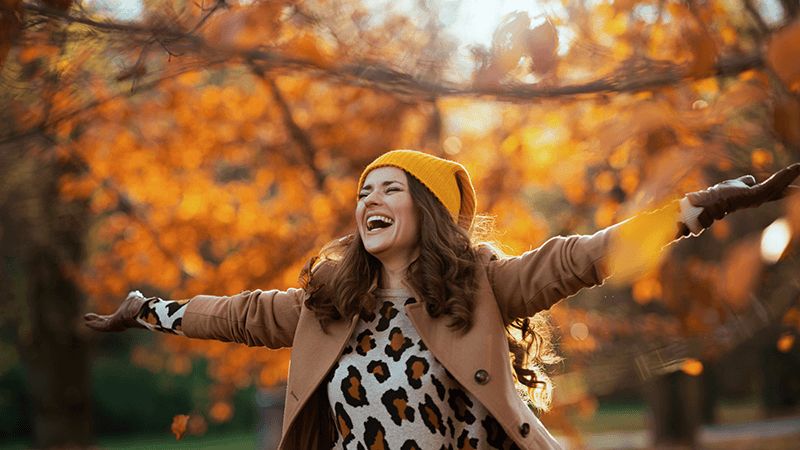 A woman smiling and holding her arms out on a scenic Autumn day