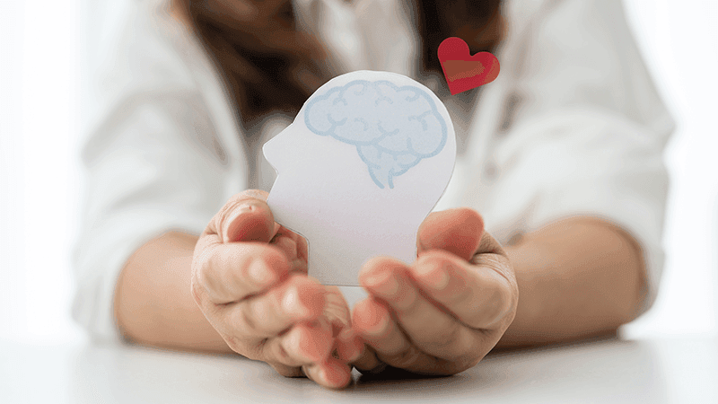 Hands cradling a paper head with brain and a heart