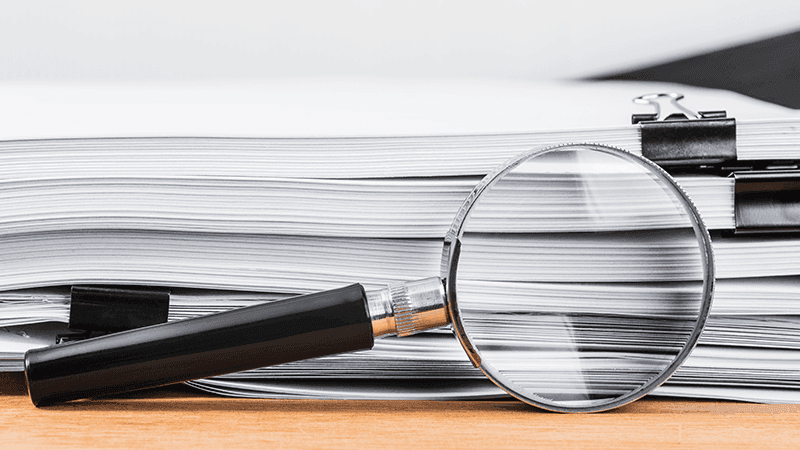 A magnifying glass next to a stack of papers.
