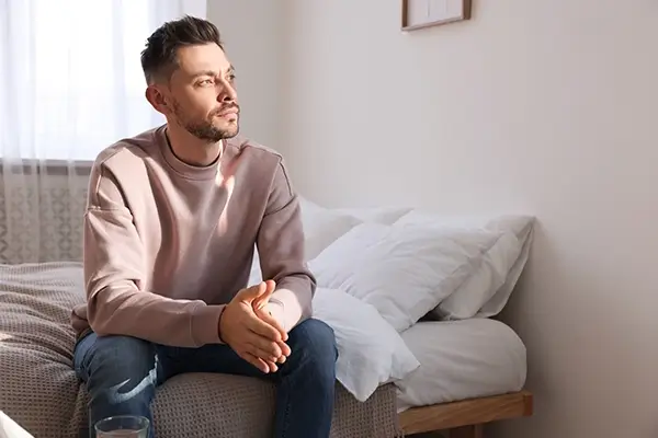 A man sitting up in a bed looking deep in thought