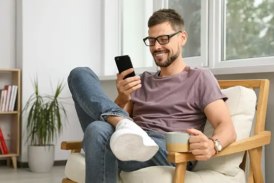 A man sitting in a chair with coffee and smiling at his phone