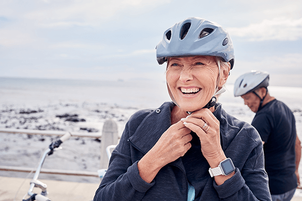 An older woman smiling and adjusting her bicycle helmet