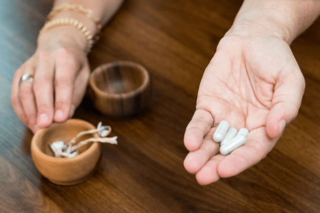 Hands holding psilocybin mushrooms and capsules