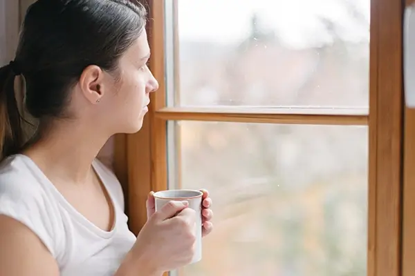 A woman with coffee looking out the window deep in thought