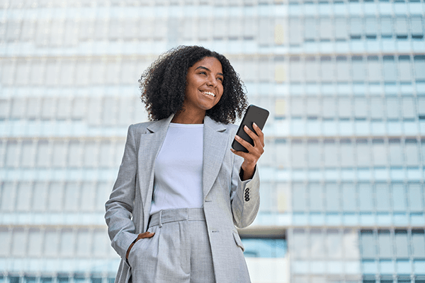 A woman standing outside in the city holding her phone up and smiling